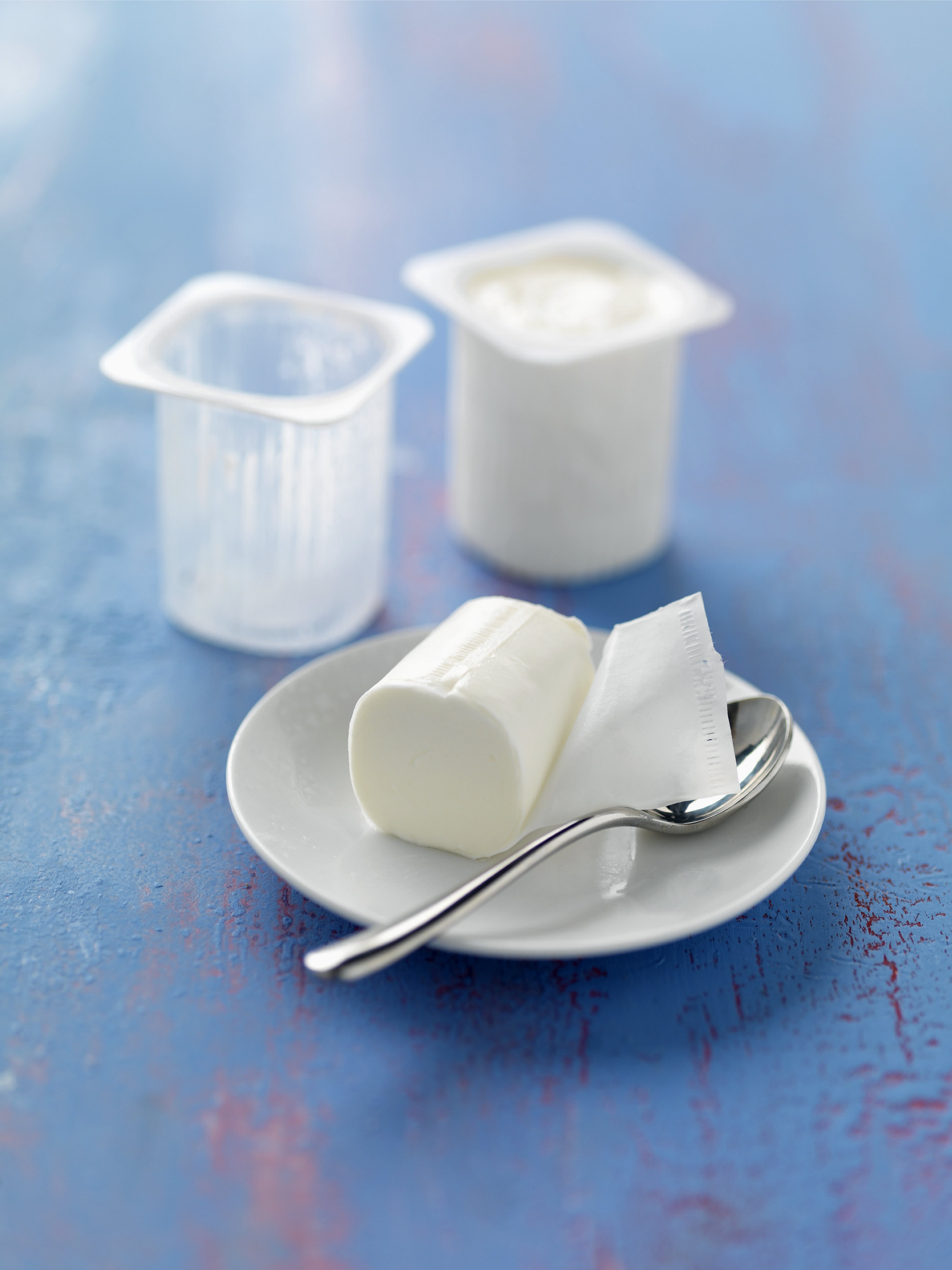 Yaourt nature moulé sur assiette blanche avec cuillère et pot en arrière-plan sur fond bleu.