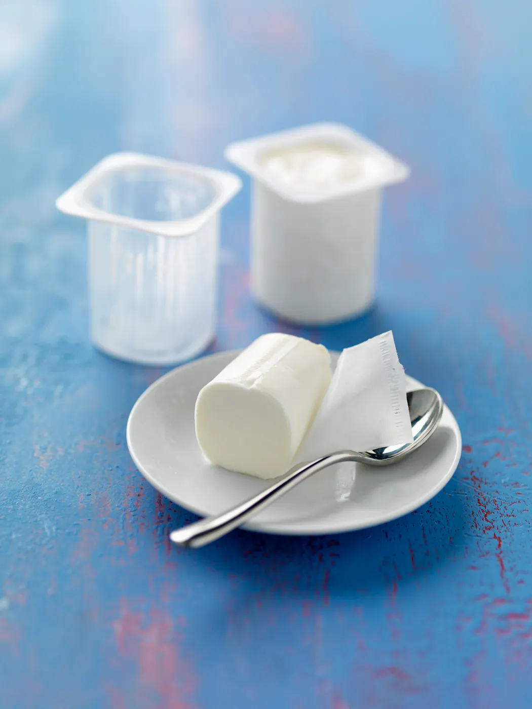 Yaourt nature moulé sur assiette blanche avec cuillère et pot en arrière-plan sur fond bleu.