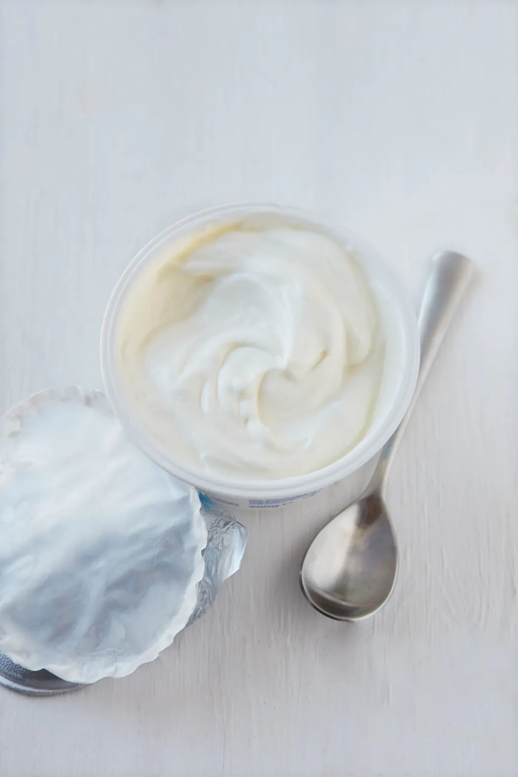 Pot de skyr avec une cuillère sur une table blanche.